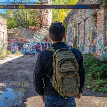 student with backpack overlooking graffiti in alley