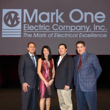 Photo of three men and one woman under Mark One logo