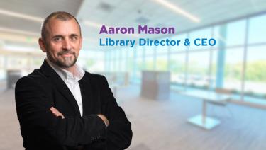 Photo of Aaron Mason wearing white shirt and black sport coat against library background with the words Aaron Mason, Library Director & CEO to the right of his head.