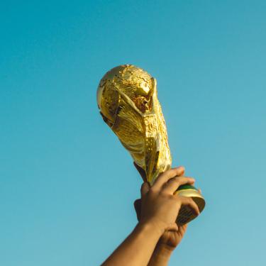 Photo of World Cup trophy being held up with sky behind.