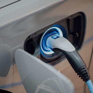 Close-up photo of electric car charger plugged into charging port on a silver car.