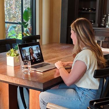 Photo of woman sitting at dining table while video chatting nurse on a laptop