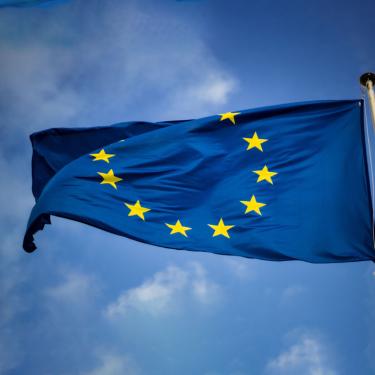 Photo of European Union flag against blue sky with whispy clouds.